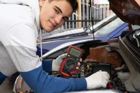 Young man using voltmeter checking voltage of car battery in car service cent Stock Photos
