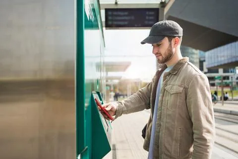 Young man validating tram ticket using mobile phone app at automatic ticket.. 스톡 사진