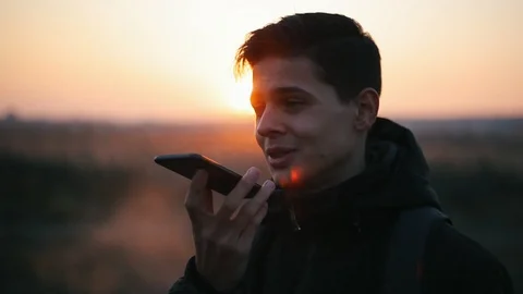 Young man vapeing and talking on the phone outdoors at sunset.Closeup Video stock 98749699