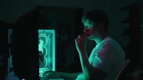 Young man vaping electronic cigarette working on computer at night, surrounded Stock Footage 317165873