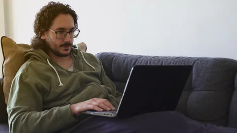 Young man in video call talking to laptop on the sofa Stock Footage 164906143