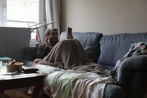 A young man on a video call, while resting on the sofa Stock Photos