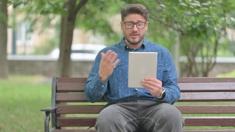 Young Man Video Calling on a Tablet Outdoor on Bench Stock-Footage 311370592