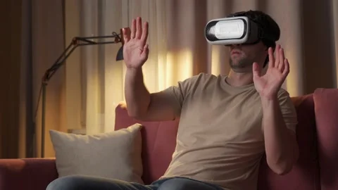 Young man in virtual reality glasses sitting on the sofa in the living room 스톡 동영상 211639323