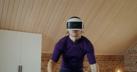 Young man in virtual reality glasses is exercising on an exercise bike, indoor Video stock 233775877