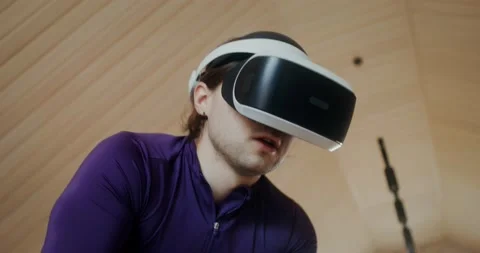Young man in virtual reality glasses is exercising on an exercise bike, indoor Video stock 233776844