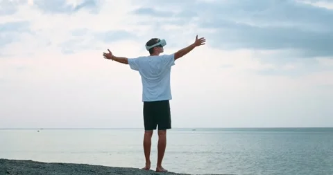 Young man in virtual reality glasses at sunset, raises his hands in the air Stock Footage 243585671