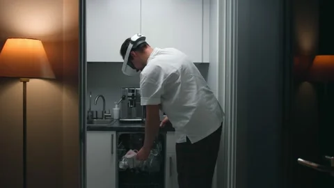 Young man in virtual reality goggles unload dishwashing machine in small kitchen Stock Footage 195944430