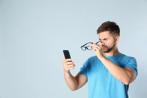 Young man with vision problems using smartphone on grey background, space for Foto stock