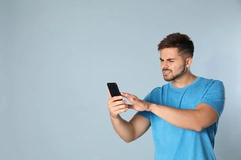 Young man with vision problems using smartphone on grey background, space for Stock Photos