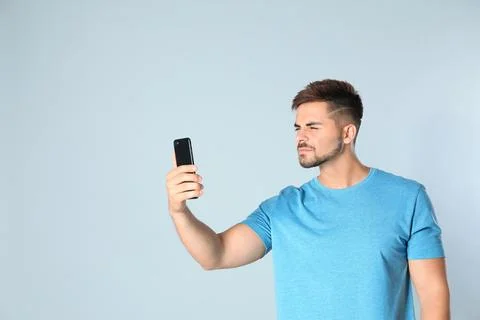 Young man with vision problems using smartphone on grey background, space for Stock Photos