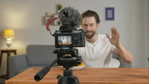 A young man, a vlogger makes a video, he sits at a table in front of the camera 스톡 동영상 129788561