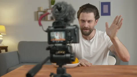 A young man, a vlogger makes a video, he sits at a table in front of the camera Stockbeeldmateriaal 130331967