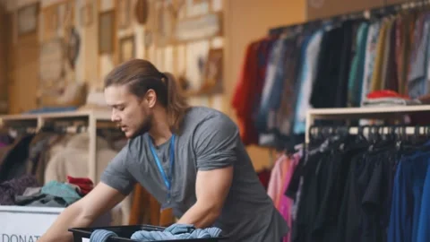 Young man volunteer sorting and unpacking clothes in plastic boxes Video stock 143573992