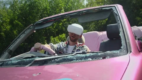 Young man in vr headset imagines he is driving broken pink car and having fun Stock Footage 236847998