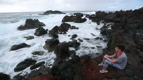 Young man waching the ocean hitting the rocky shore Stock Footage 64257802