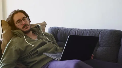 Young man waking up after nap while working with laptop on the sofa Stock Footage 164906344
