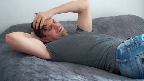 Young man is waking up in bed wearing in jeans and t-shirt after party. Video stock 153533317