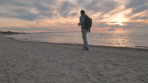 Young man walking alone on the sandy beach along the sea at sunset Stock Footage 219919249