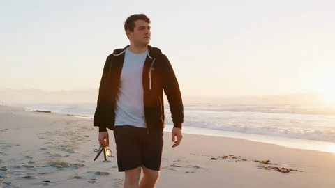Young Man Walking Along Beach As Sun Rises Over Ocean Stock Footage