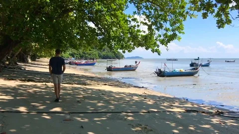 A young man walking along the beach with anchored fishing boats Stock-Footage 101471321
