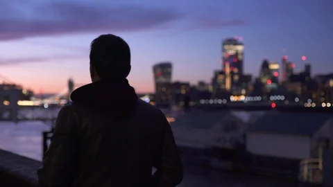 Young man walking alongside Thames river with City of London skyline view Video stock 121618455
