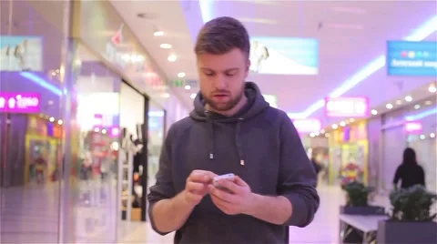 Young Man Walking and Looking at the Phone in a Mall. Stock Footage 47977320