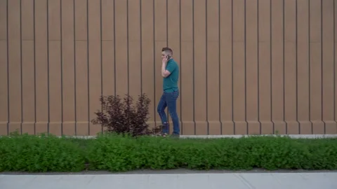A young man is walking and talking on the phone. A man walks near the building Stock-Footage 132190460