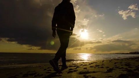 Young man walking on the beach in beautiful sunset at the sea.  Cloudy sky, sun Stock Footage 80388246