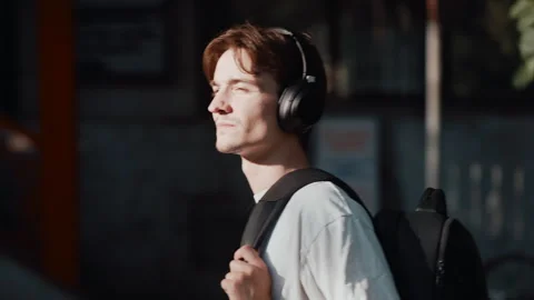 Young man walking in city sunlight listening to music with headphones and Видео 344045123