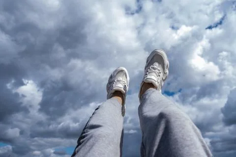 Young man walking in the clouds. Concept, white sneakers on a blue background Stock Photos