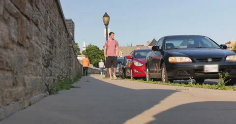 Young Man Walking Down City Street by Stone Wall Dolly Shot, 4K Stock Footage 65118542