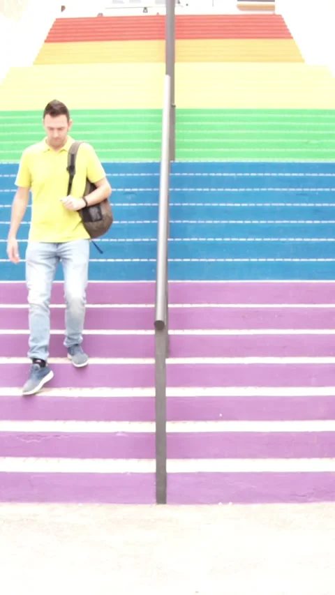 Young Man Walking down Colorful Stairs. Descending Rainbow staircase in the Stock Footage 220525020