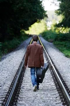Young man walking down train tracks with guitar Stock Photos