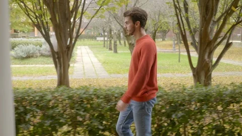Young man walking fast at park, stopping and staring at camera Stock Footage 121157542