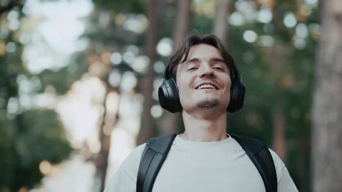 Young man walking in forest smiling, listening to music with headphones and Stock Footage 340858723