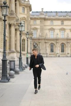 Young man walking near building in Paris, wearing black suit. Fotos de archivo