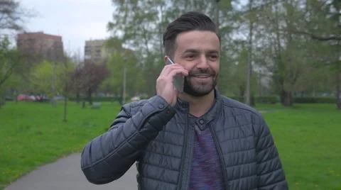 Young man walking in the park and talking on the phone. Video stock 62735876