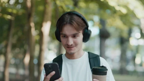 Young man walking in park smiling, talking and holding coffee cup Stock Footage 339216040