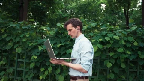 Young man walking at park using laptop with headphones and sit down on bench Stock Footage 77168954