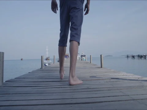 Young Man Walking on Pier Toward Ocean. Boy walks on wooden pier Stock Footage 70712499