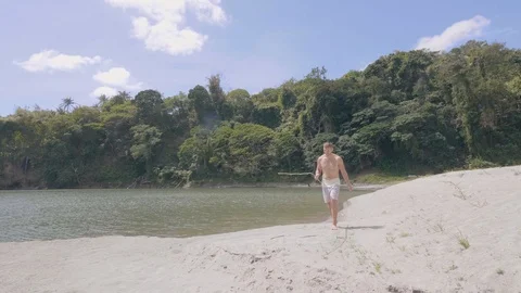 Young man is walking on sand beach on the lake with handmade fishing rod. Stock Footage 112469345