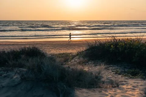 Young man walking on a sandy beach at sunset. Tourist walking on the beach ba Stock Photos