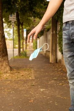 Young man walking on a sidewalk throwing away a surgical mask Stock Photos