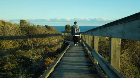 Young man walking slowly along a boardwalk during the late afternoon Stock Footage 317926690