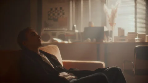 Young Man Walking in Softly Lit Room, Leaning Back on Couch in Deep Thought Stock Footage 307548710