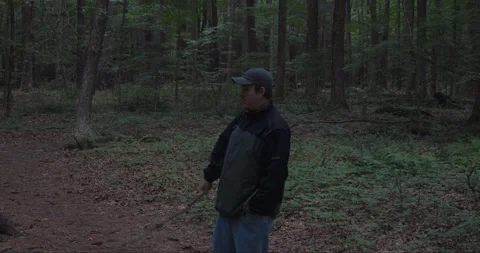 Young man walking through the woods, playfully using a walking stick. Stock Footage 313948861