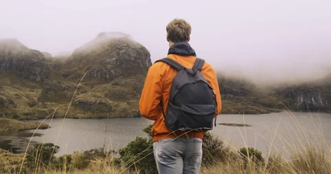 Young man walking towards epic view of lake and mountains Stock Footage 87211962