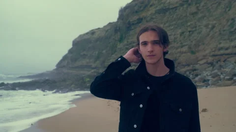 Young man walks alone on the empty ocean beach on the cloudy rainy weather. Stock Footage 306636417