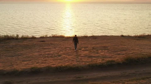 A young man walks along the seashore at sunset. In the frame there is a cliff Stock Footage 161306565